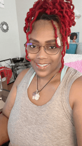 a woman with red dreadlocks is wearing glasses and a grey tank top