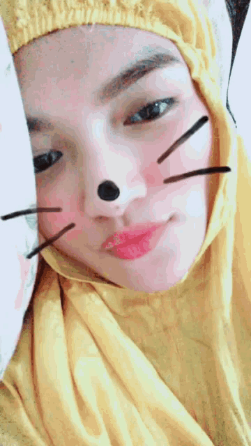 a woman wearing a yellow scarf has a cat face painted on her nose