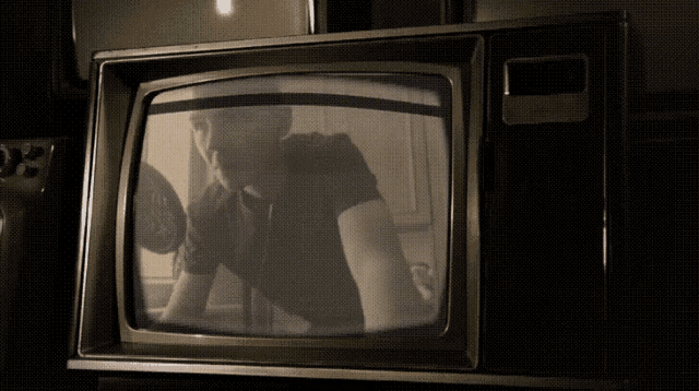 a black and white photo of a man sitting in front of a television
