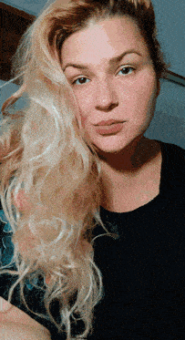 a woman with blonde hair and a black shirt looks at the camera
