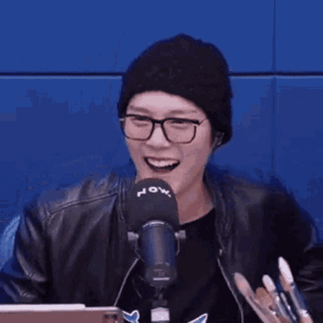 a man wearing glasses and a beanie is standing in front of a microphone holding a brush .