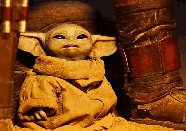 a baby yoda is sitting in the sand next to a pair of boots