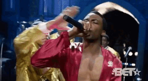 a man is singing into a microphone while wearing a red robe .
