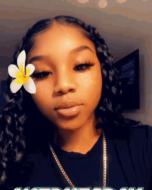 a girl with a flower in her hair is wearing a black shirt and a necklace