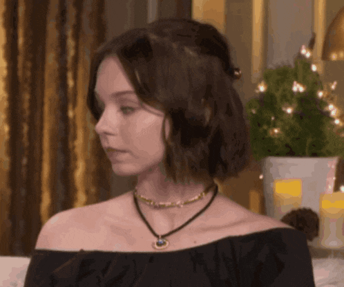 a woman wearing a black off the shoulder top and a choker is sitting on a couch .