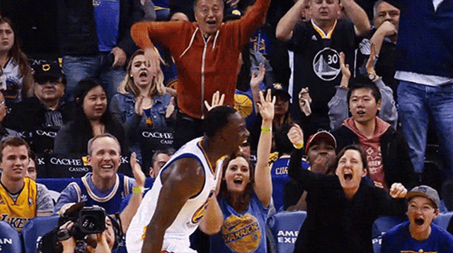 a man in a golden state warriors jersey stands in front of a crowd of people