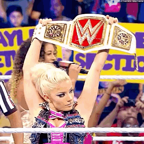 a woman is holding up a wrestling championship belt in a ring