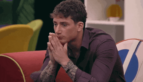 a man is sitting on a red couch with his hands folded