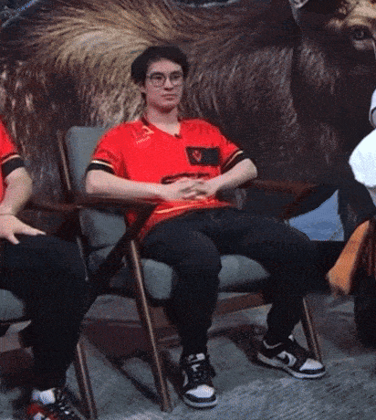 a man in a red shirt is sitting in a chair in front of a painting of a bear .