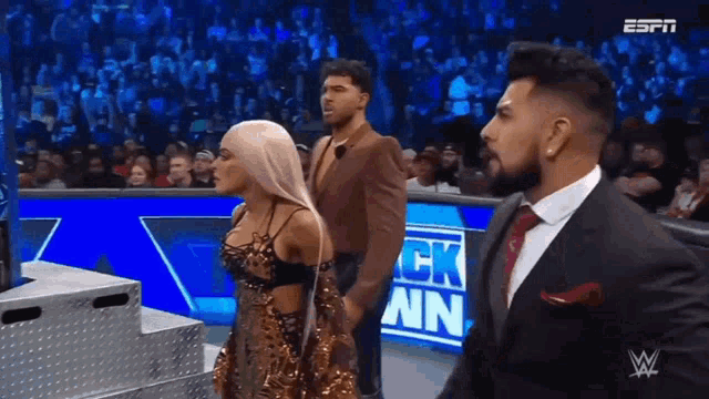 a man in a suit and tie is standing next to a woman in a dress on a wrestling show .