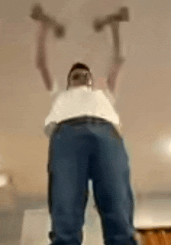 a man is holding two hammers over his head and looking up at the camera .