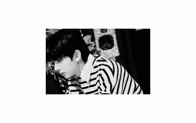 a black and white photo of a young man wearing a striped shirt and earrings .