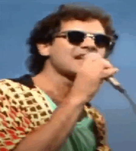 a man singing into a microphone wearing sunglasses and a colorful shirt