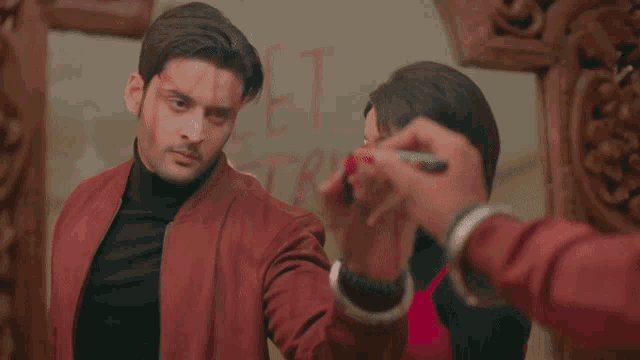 a man in a red jacket is standing next to a woman who is writing on a wall