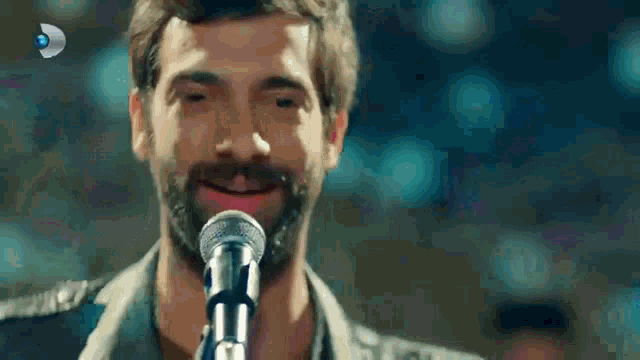 a man with a beard is singing into a microphone with the letter d in the corner