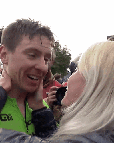 a woman kisses a man on the cheek who is wearing a green shirt with the letters eia on it