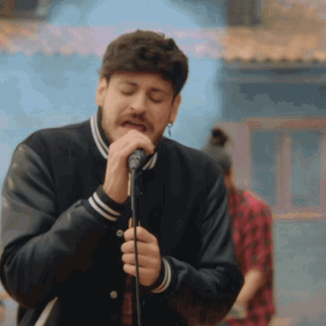 a man singing into a microphone while wearing a varsity jacket