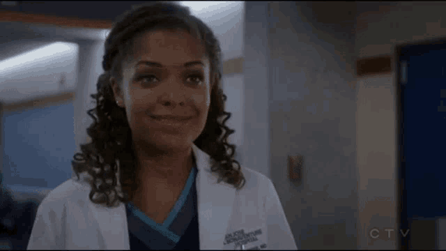 a woman in a lab coat and scrubs is smiling in a hallway .