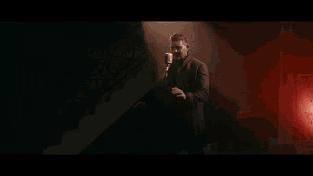 a man in a suit is singing into a microphone in a dark room with red lights .