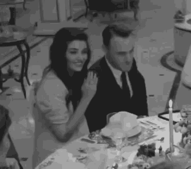 a black and white photo of a man and a woman sitting at a table with candles .