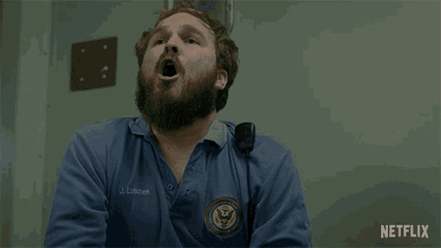 a man with a beard is wearing a blue shirt with the name j. lubbak on it