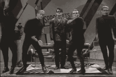 a group of men in black jumpsuits are dancing on a rug in a room .
