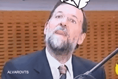 a man with a beard and tie is standing in front of a microphone and making a funny face .