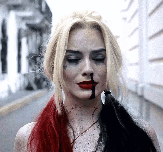 a woman with red and black hair is wearing a harley quinn costume and has blood coming out of her nose .