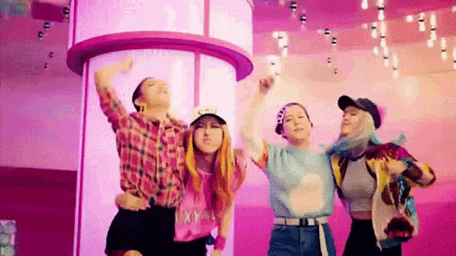 a group of young women are standing next to each other in front of a purple pillar .