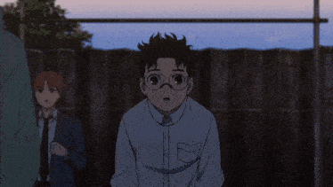 a boy wearing glasses is standing in front of a wooden fence