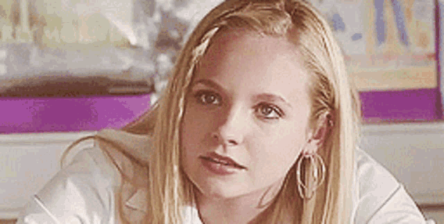 a woman wearing hoop earrings and a white shirt looks at the camera