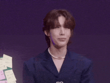 a man wearing a pearl necklace and a blue jacket is making a funny face .