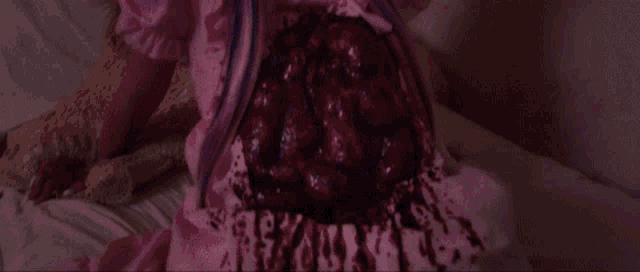 a woman in a pink dress is laying on a bed with blood coming out of her belly