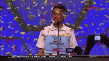 a boy with the name arvind on his shirt is standing in front of a microphone
