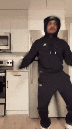 a man in a black nike hoodie is dancing in front of a refrigerator