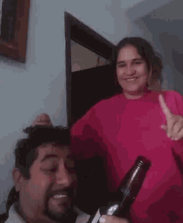 a man and a woman are posing for a picture while the woman is holding a bottle .