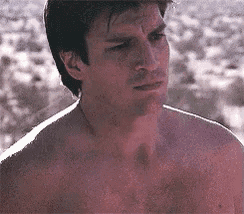 a man without a shirt is standing in the desert looking at something .