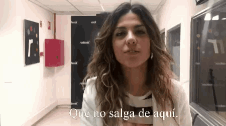 a woman is standing in a hallway with the words que no salga de aqui below her