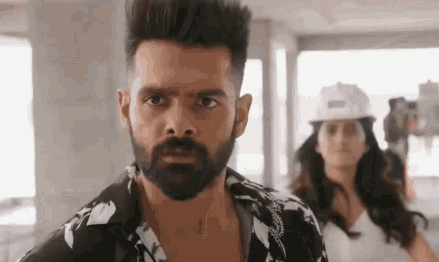 a man with a beard and a woman in a hard hat are standing next to each other in a building .