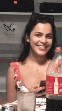 a woman is smiling while sitting at a table with a bottle of coca cola in front of her .