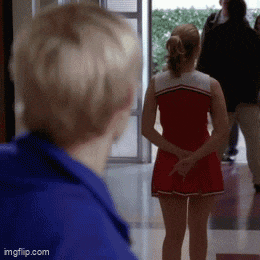 a cheerleader in a red dress is standing next to a man in a blue jacket in a hallway .