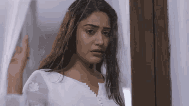 a woman in a white top looks out a window