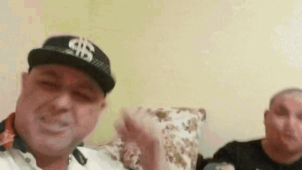 a man wearing a hat with a dollar sign on it is sitting next to another man