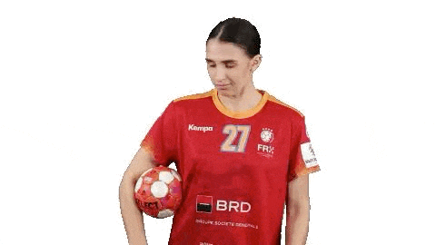 a woman in a red jersey is holding a handball in her hand .
