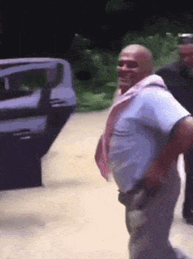 a man with a pink scarf around his neck is standing in front of a car