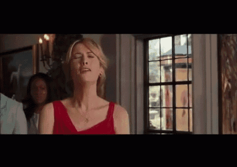 a woman in a red dress is standing in front of a window and making a funny face .