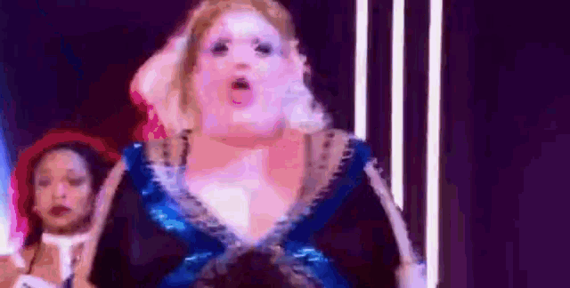 a woman in a blue dress is singing on a stage while another woman stands behind her .