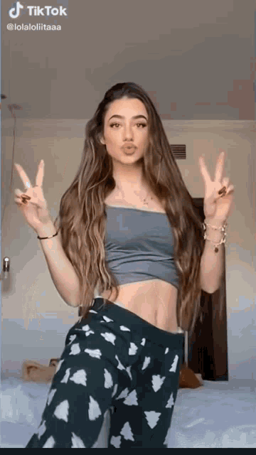 a woman in a crop top and pajama pants giving the peace sign