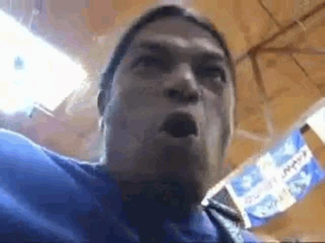 a man in a blue shirt is making a funny face in front of a flag .