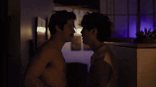 a couple of men without shirts are having sex in a dark room